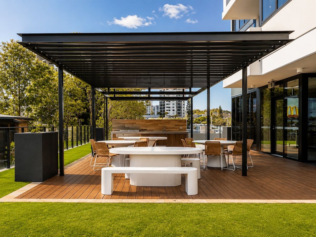 An outdoor patio with a wooden deck, white furniture, and a black pergola.