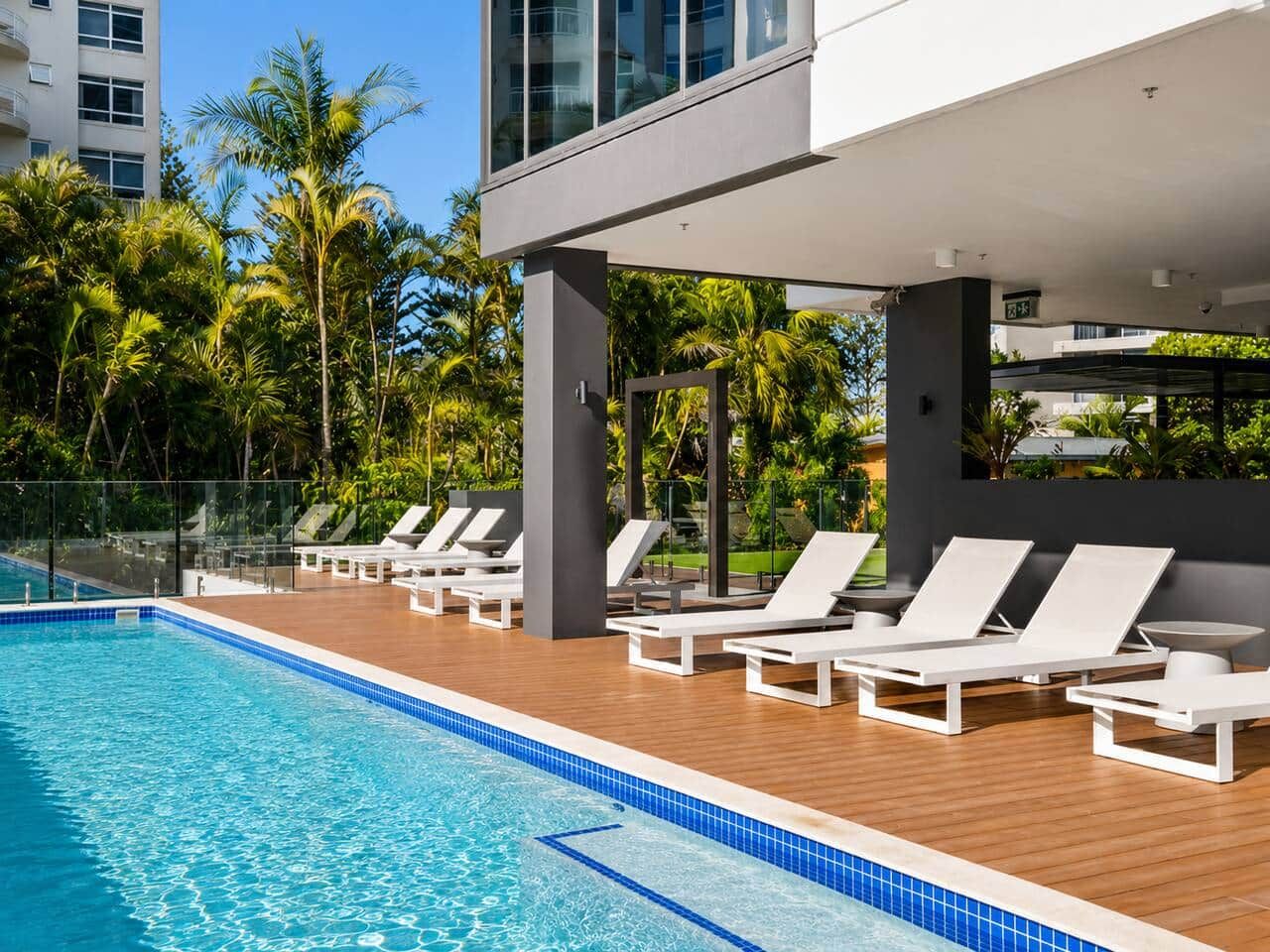A swimming pool with lounge chairs and a modern building in the background.