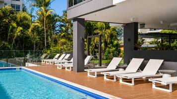 A swimming pool with lounge chairs and a modern building in the background.