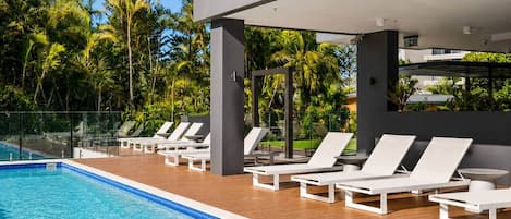 Una piscina con sillas de descanso y un edificio moderno al fondo.