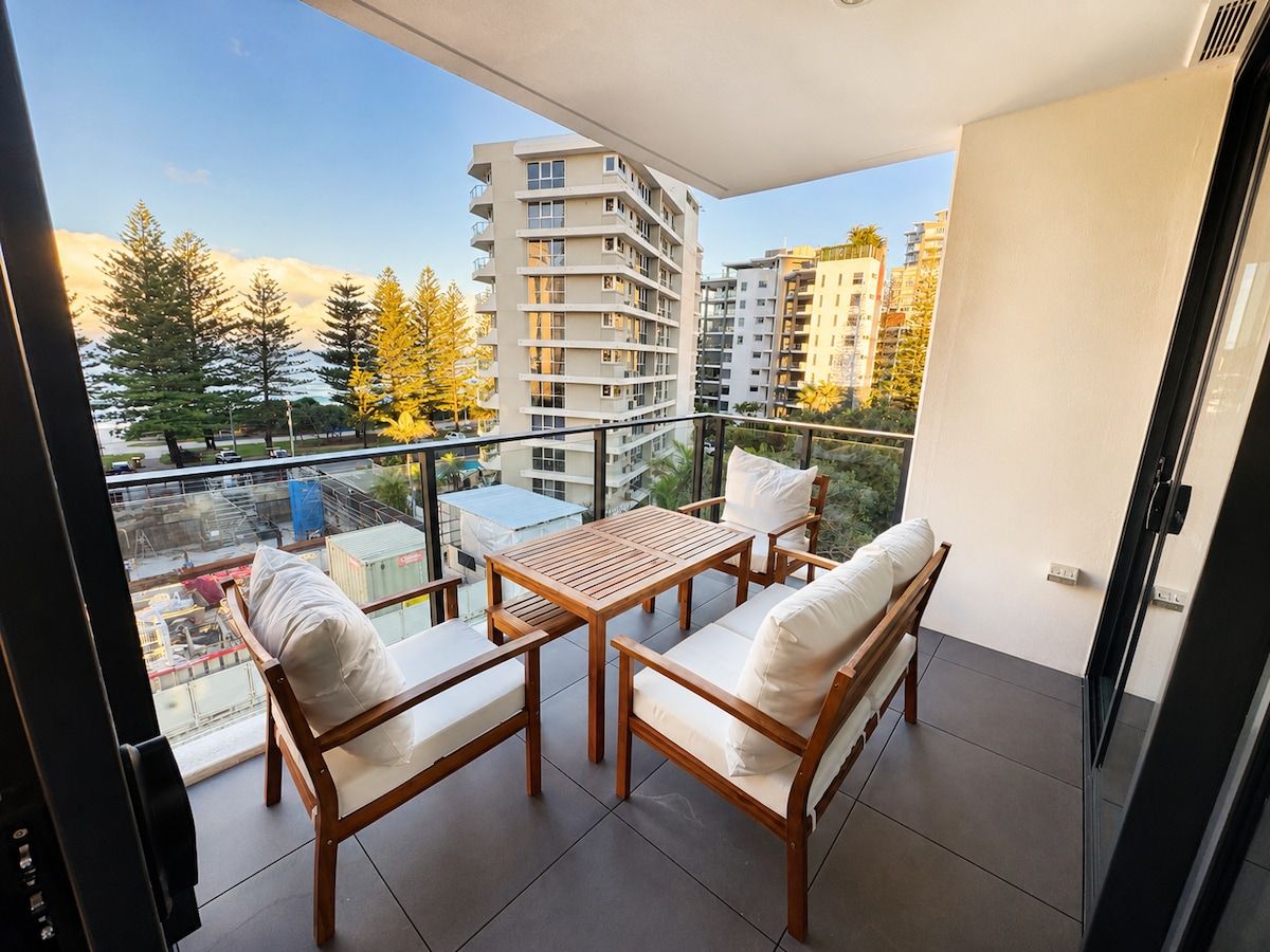 Een balkon met een tafel en stoelen, uitzicht op gebouwen en een heldere lucht.