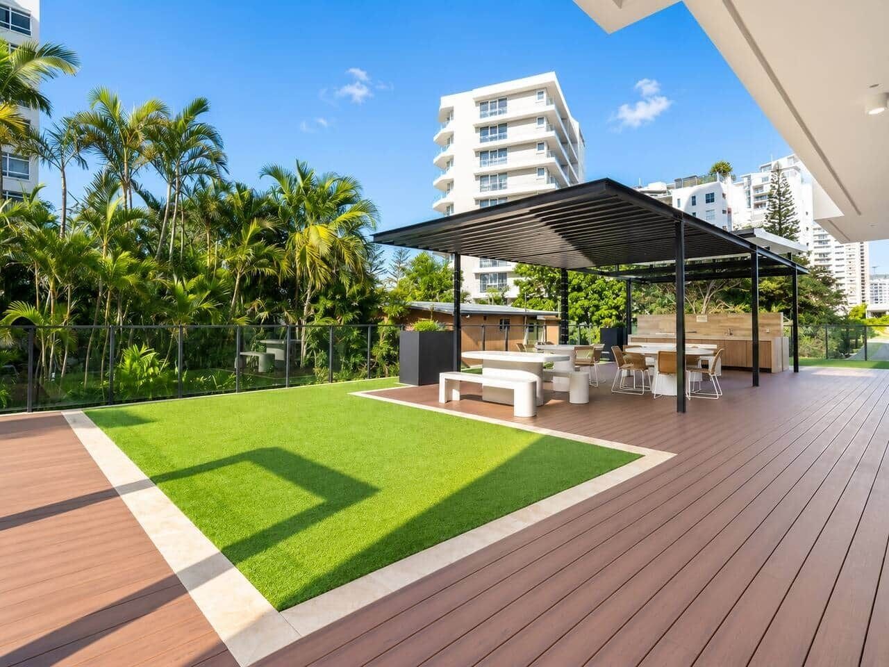 A modern outdoor patio with a wooden deck, a grassy area, and a covered seating area with tables and chairs.