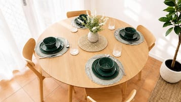 A round wooden dining table with green plates, silverware, and a centerpiece.