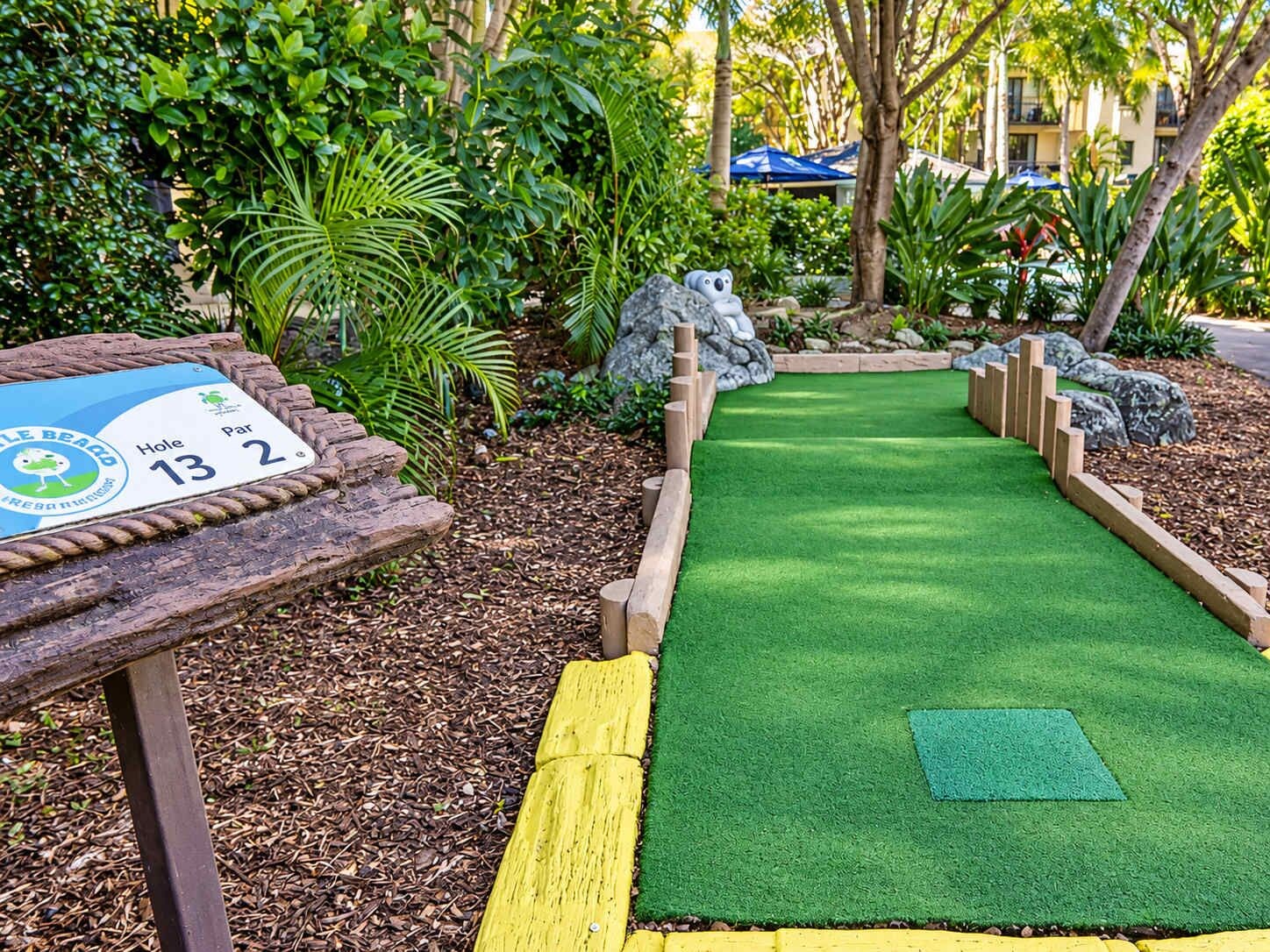 A miniature golf course with a wooden sign indicating hole 13 and par 2.