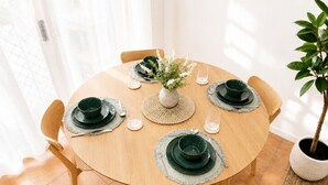 Ein runder Holztisch mit grünen Tellern, Besteck und einer zentral platzierten Vase mit weißen Blumen.