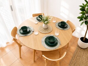 Ein runder Holztisch mit grünen Tellern, Besteck und einer zentral platzierten Vase mit weißen Blumen.