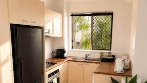 Eine kleine Küche mit einem schwarzen Kühlschrank, einer Spüle und einem Fenster mit Blick auf Grünflächen.