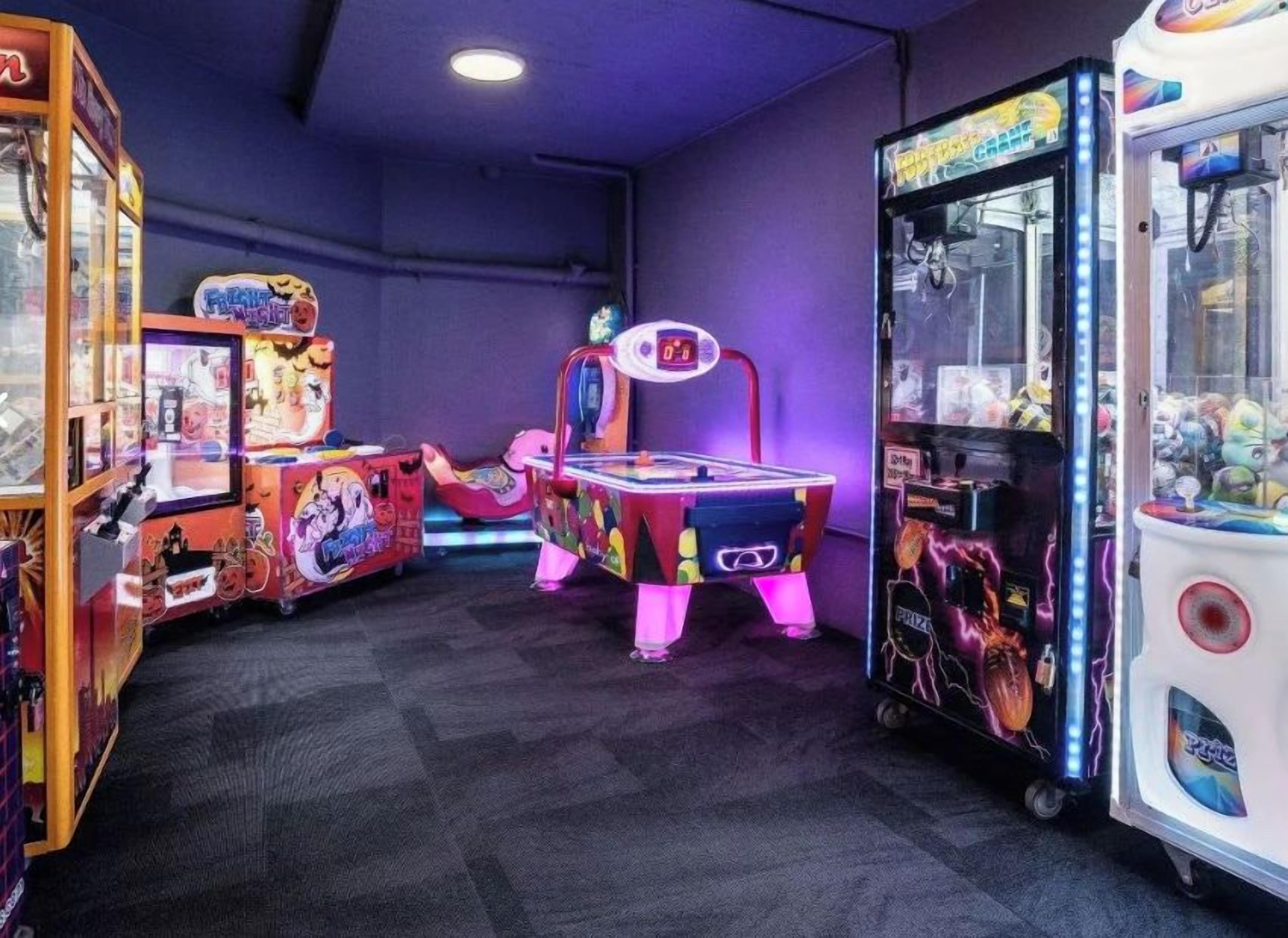 A room with arcade games, including claw machines and a racing game.