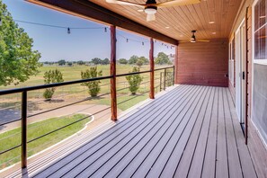 A wooden balcony with a view of a green field and a road.
