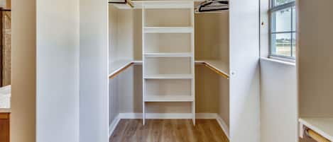 Un dressing accessible sans porte, doté d’un plancher en bois et d’étagères blanches.