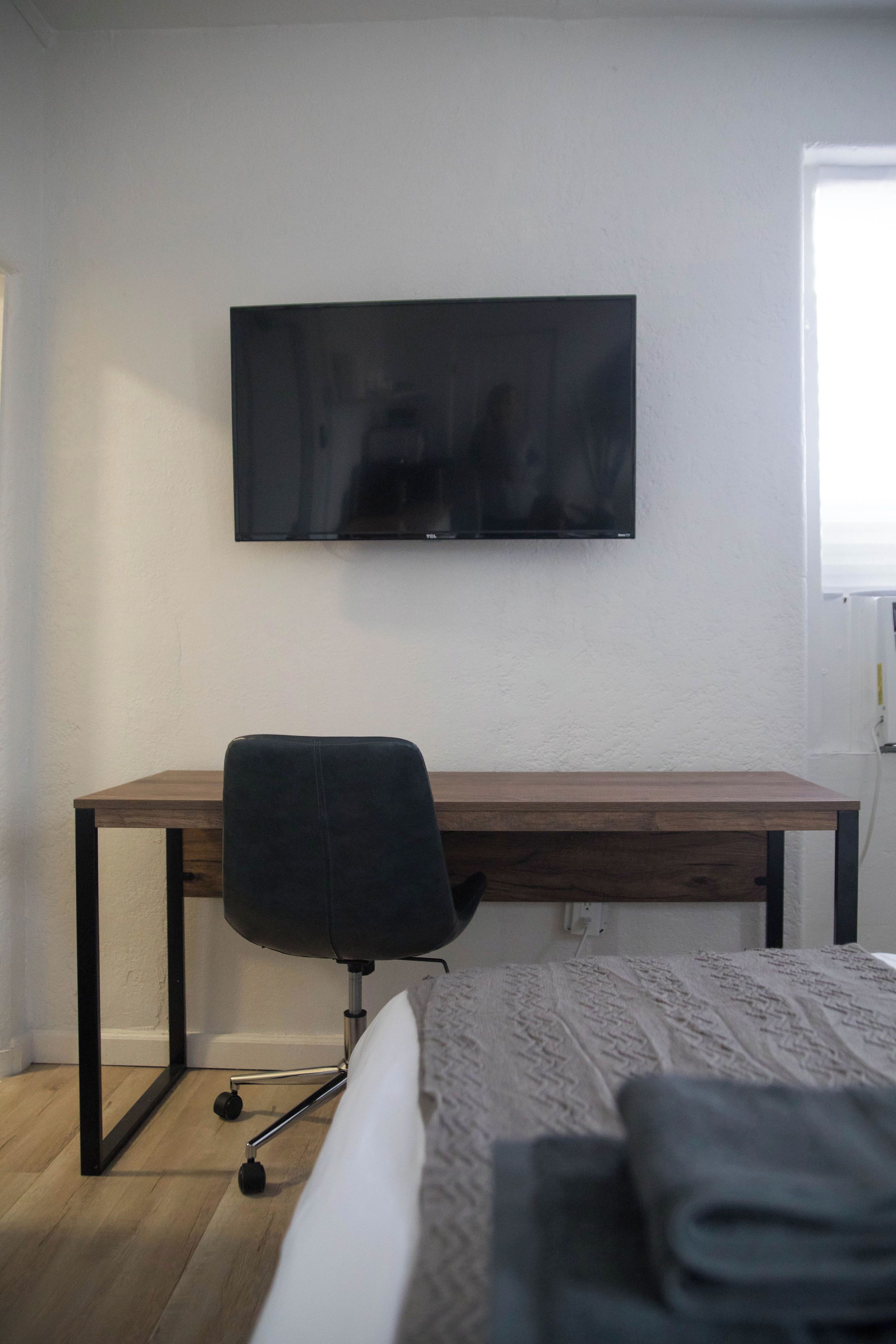 A bedroom with a bed, a desk, and a television mounted on the wall.