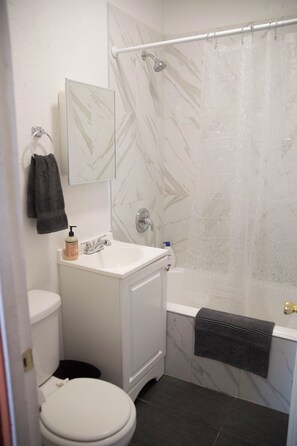A bathroom with a white toilet, a sink with a mirror above it, a shower with a glass door, and a towel hanging on the wall. - Cozy studio in fantastic Los Angeles with refreshing AC (Los Angeles)
