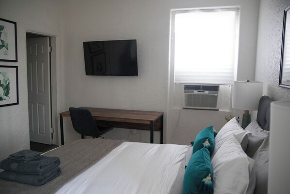 A hotel room with a bed, a desk, a chair, a TV, and an air conditioning unit. - Cozy studio in fantastic Los Angeles with refreshing AC (Los Angeles)