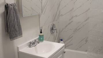 Een badkamer met een witte wastafel, een spiegel, een handdoekhouder, een douche en een wand met marmerlook.