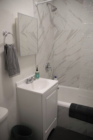 A bathroom with a white sink, a mirror, a towel rack, a shower, and a marble-patterned wall.