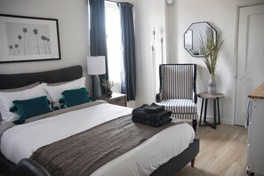 A neatly made bed with a striped chair and a small table with a vase. - Cozy studio in fantastic Los Angeles with refreshing AC (Los Angeles)