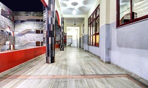 Un pasillo con piso de mármol, paredes rojas y blancas, y una escalera a la izquierda.