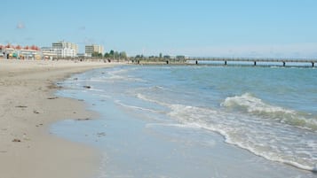 A beach with a pier extending into the water, buildings in the background, and a clear sky.