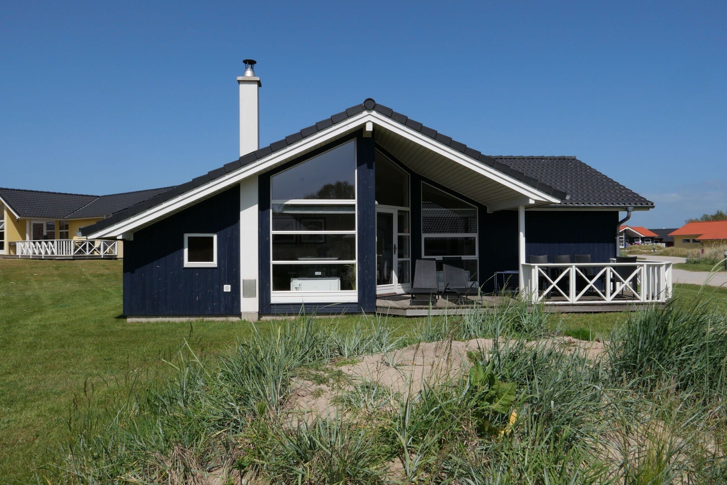 A modern house with a large deck, a chimney, and a clear sky.