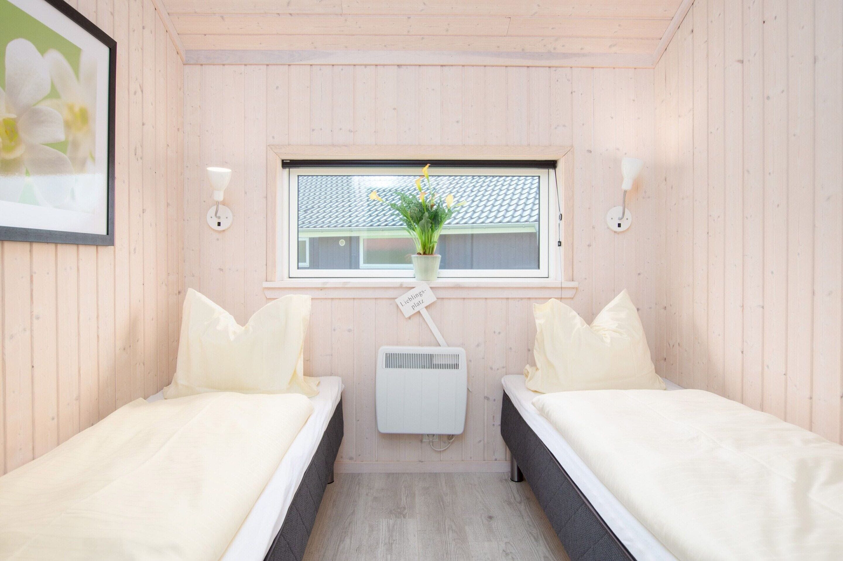 A room with two beds, a window with a view of a building, a wall-mounted air conditioner, and a framed picture on the wall.