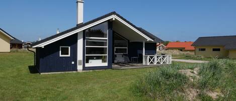 A single-story house with a sloped roof, a chimney, and a covered porch with outdoor furniture.