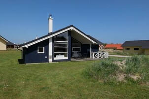 Einbungalow mit geneigtem Dach, Schornstein und überdachter Veranda mit Gartenmöbeln.