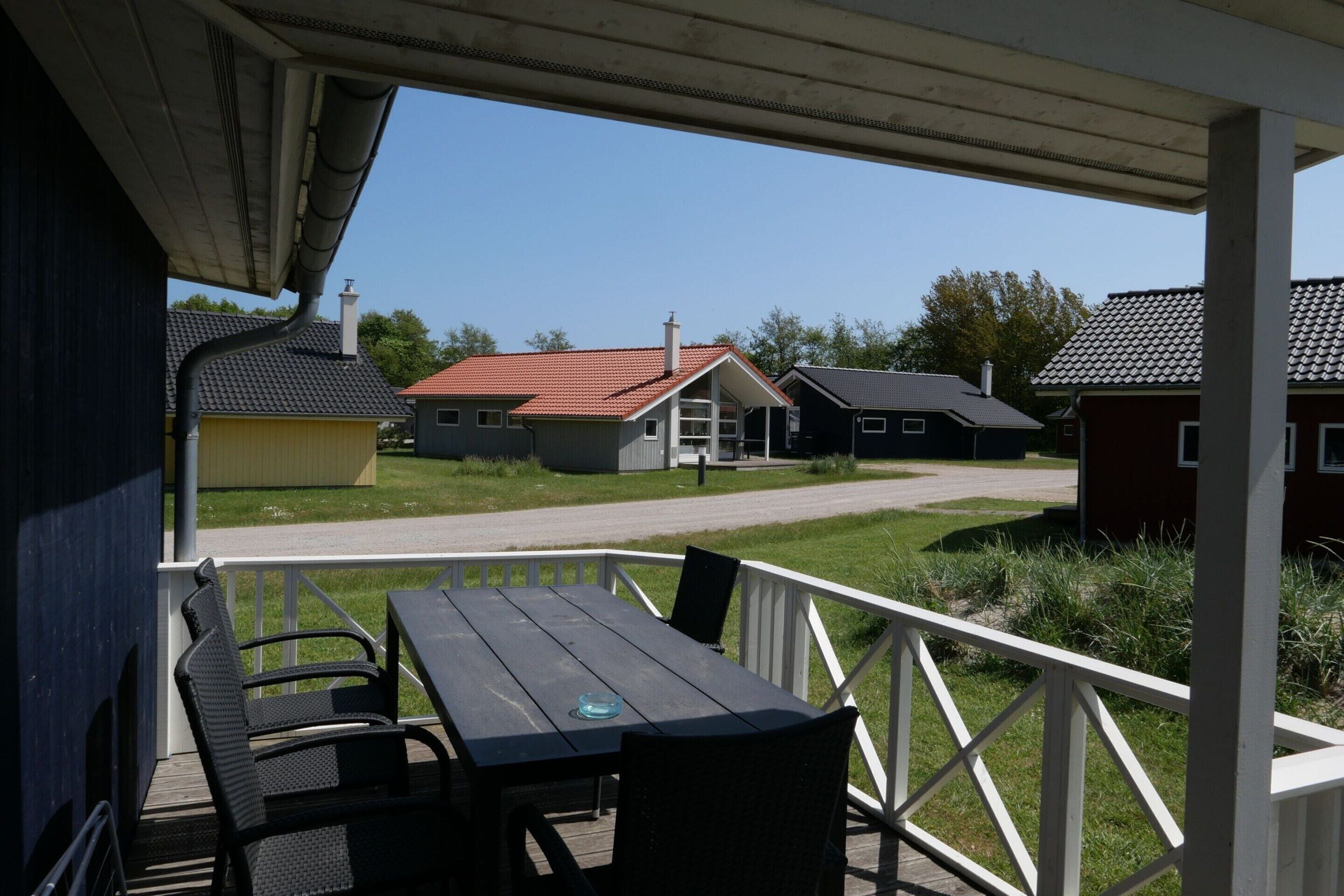 Ett takförsett utomhusområde med bord och stolar, med utsikt över en bostadsgata med hus.