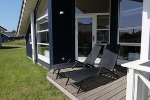 A deck with two lounge chairs and a glass door leading to a covered area. - Ostsee-ferienparadies fur 8 Personen (Grossenbrode)