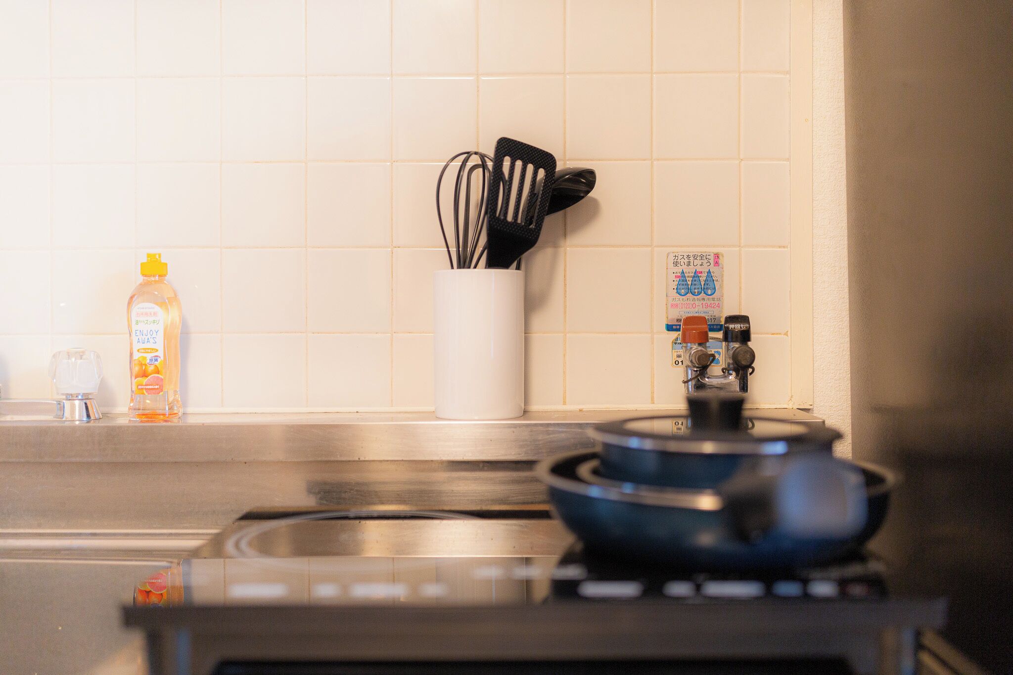 A kitchen with a stove, a pot, a bottle of orange juice, a white container with utensils, and a water safety sign.