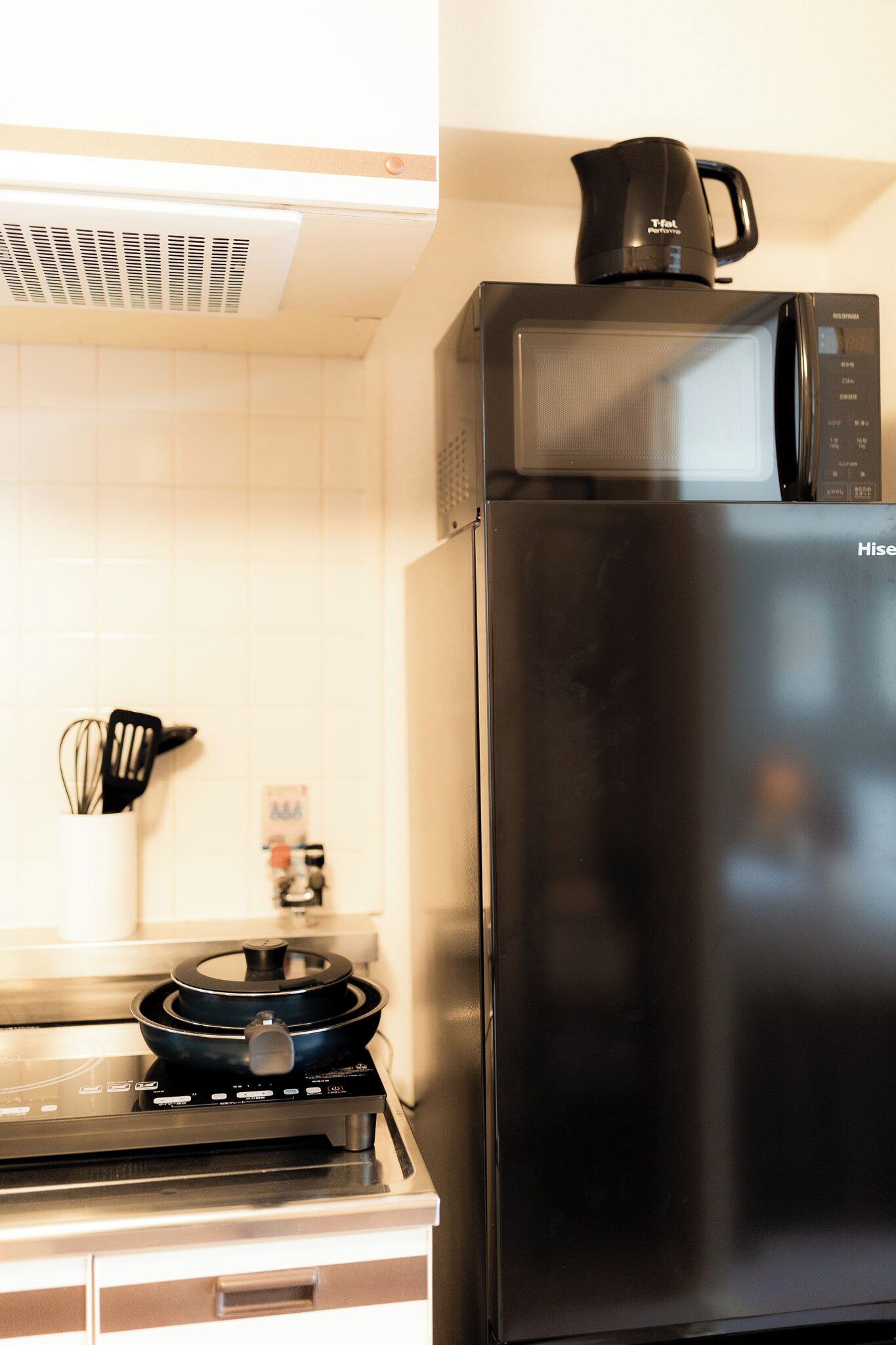 A kitchen with a black microwave, a kettle, and a stove.