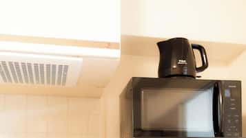 A kitchen with a black microwave, a kettle, and a stove.