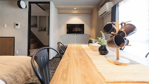 Una habitación con una mesa de comedor de madera, sillas, un televisor en la pared y una escalera que lleva a otra zona.