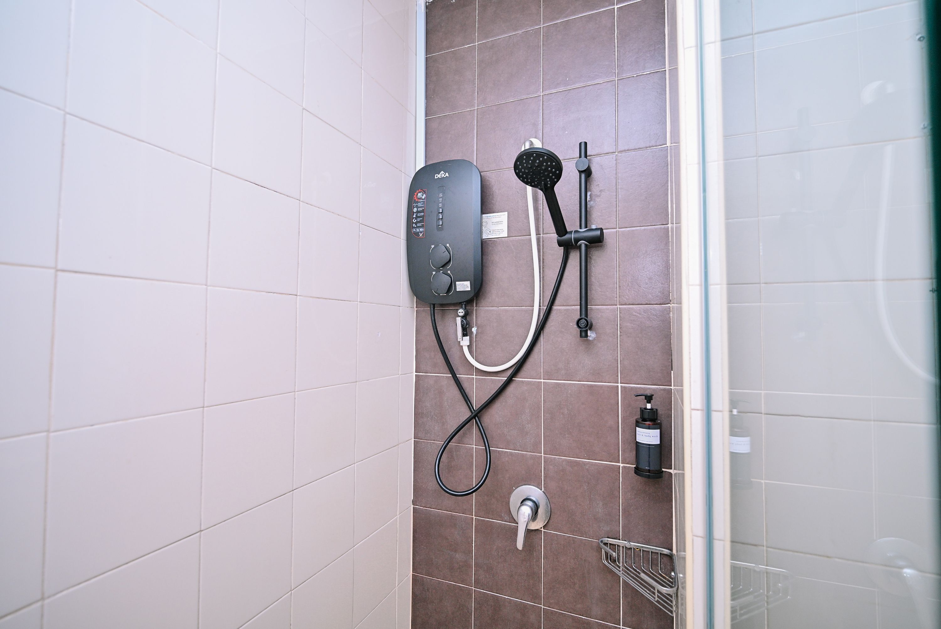 A bathroom with a shower unit, a handheld showerhead, a bottle of shampoo, and a towel rack.
