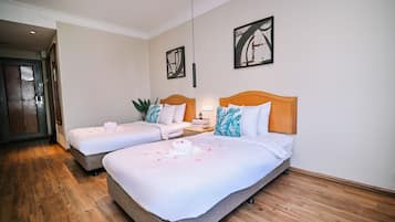 A hotel room with two beds, a wooden floor, and artwork on the walls.