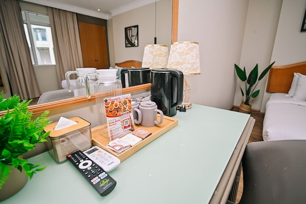Habitación de hotel con cama, escritorio con cafetera, control remoto y bandeja con menú.