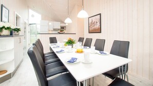 A modern dining area with a long table, black chairs, white plates, and a white ceiling. - Strandvilla mit 4 Schlafzimmern (Grossenbrode)
