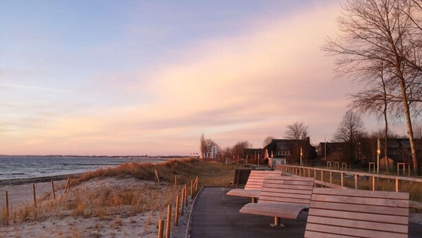 A wooden boardwalk leading to a beach with benches and a fence. - Strandvilla mit 4 Schlafzimmern (Grossenbrode)