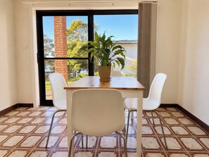 A room with a table, two chairs, a potted plant, and a view through a glass door.