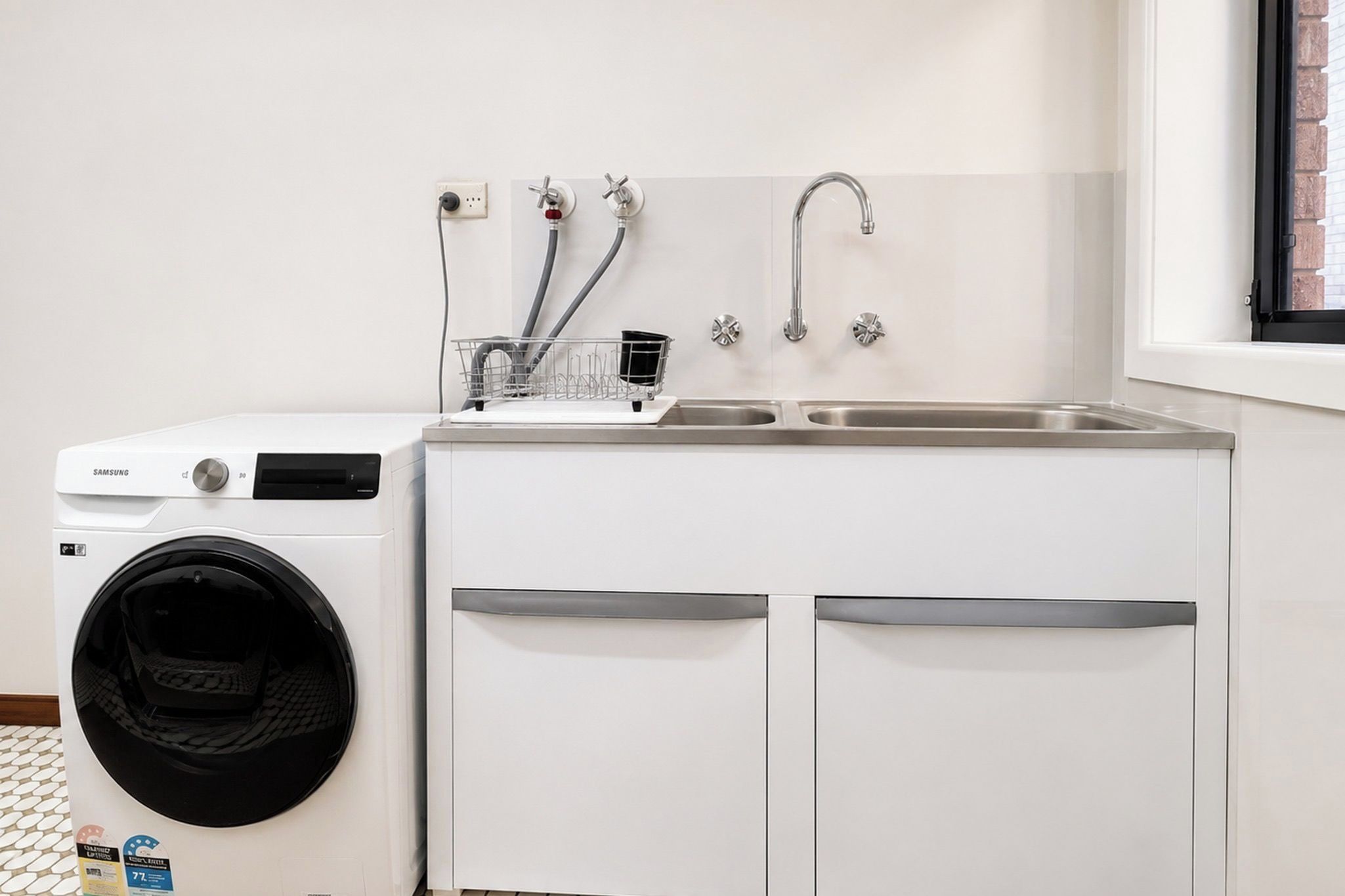 A compact laundry area with a front-loading washing machine, a sink with a faucet, and a dish rack.