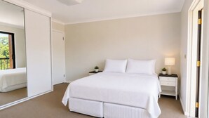 Ein Schlafzimmer mit einem großen Bett, einem Nachttisch, einer Lampe und einem Spiegel.