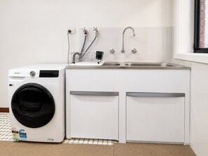 A compact laundry area with a washing machine, a sink, and a drying rack.