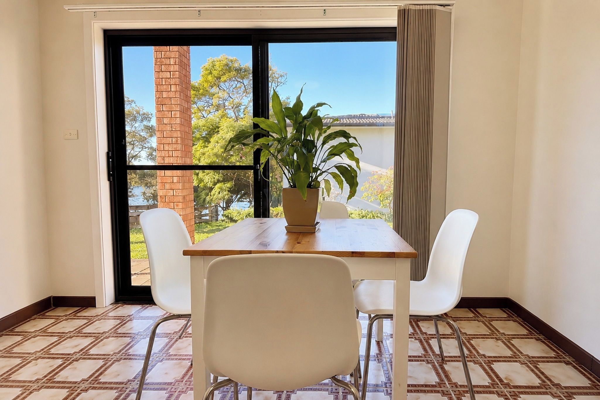 A room with a table and chairs, a potted plant, and a view through a glass door.