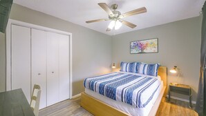 Ein Schlafzimmer mit Bett, Deckenventilator, Nachttisch und Lampe sowie einer Tür.