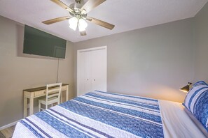 Ein Schlafzimmer mit einem Bett, einem Schreibtisch, einem Stuhl, einem Kleiderschrank und einem Deckenventilator.