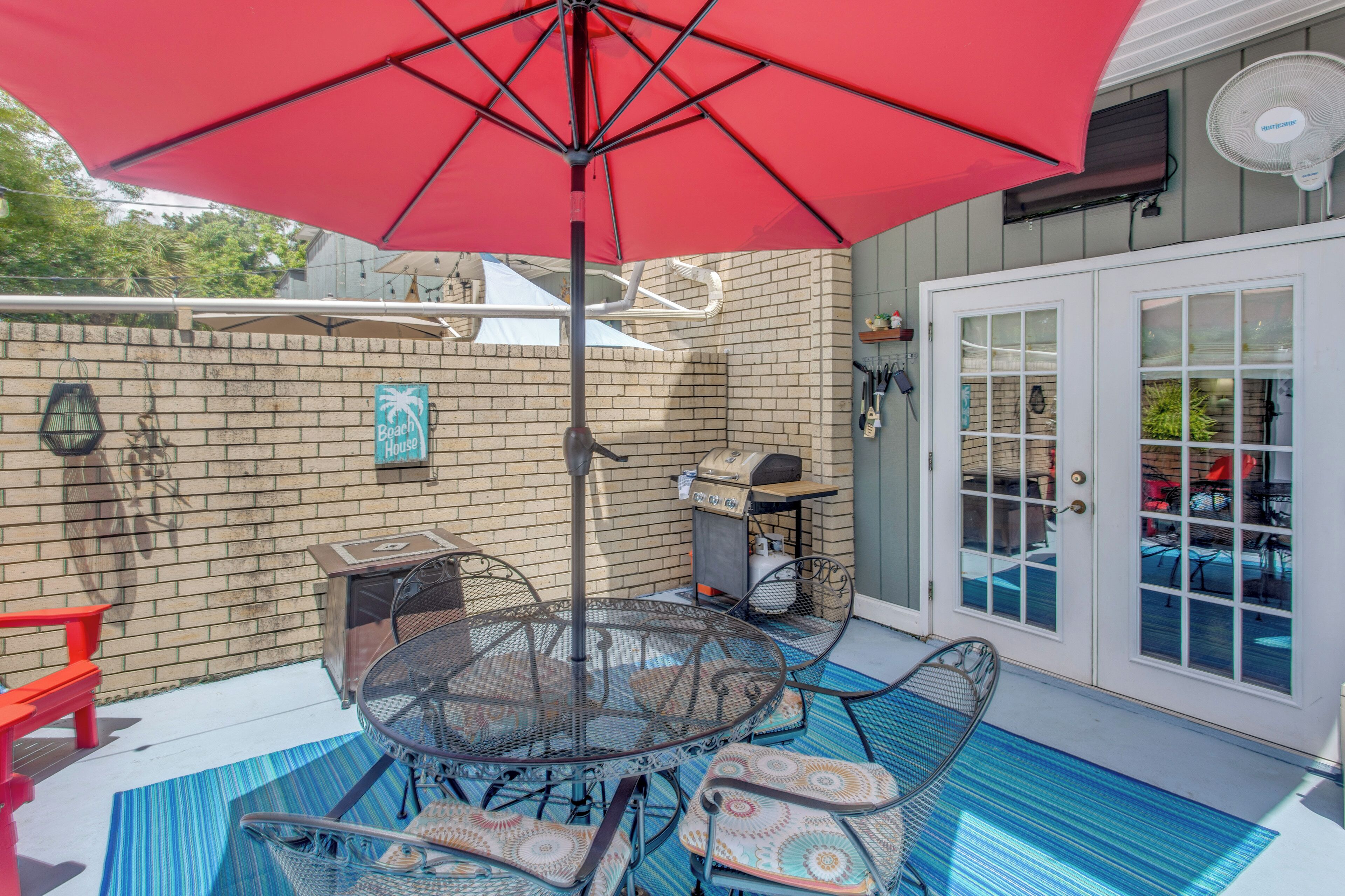 Eine Terrasse mit rotem Sonnenschirm, Grill und Gartenmöbeln.