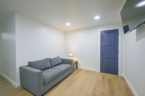 A small, sparsely furnished room with a grey sofa, a small table with a lamp, and a blue door. - Walk to Main St: Red River Lodge w/ Ski Views! (Red River)
