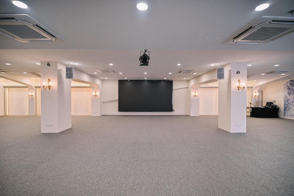 Une grande salle de conférence équipée d’une scène, de plusieurs luminaires au plafond et d’un projecteur.
