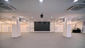 Een grote congreszaal met een podium, meerdere plafondlampen en een beamer.