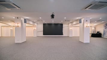 A large conference room with a stage, multiple ceiling lights, and a projector.