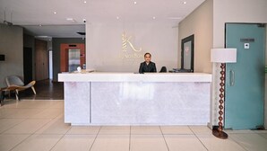 Een receptiebalie van een hotel met een modern ontwerp, een bordje 'controleruimte' en een wachtruimte met een stoel en een lamp.